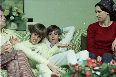 Vintage indoor family portrait from the 1970s–80s, featuring three children and an adult woman on a floral-patterned sofa. Bo...
