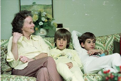 Vintage indoor portrait of a woman and two boys on a floral-patterned sofa, mid-1970s. The woman wears a light-colored blouse...