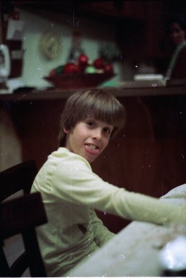 Vintage black-and-white photo of a young girl in a 1960s-style dress, seated at a wooden table with a bowl of fruit (apples) ...