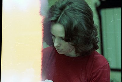 Vintage portrait featuring a person with short, wavy hair in a red top, shot through a window with lens flare. Warm light and...