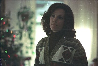 Vintage portrait of a woman in a 1970s-style sweater with geometric patterns, standing near a decorated Christmas tree. Soft ...