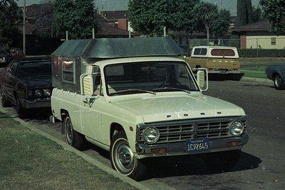 1970s Ford E-Series pickup with pop-up camper parked in a residential area. White exterior with chrome accents, California li...