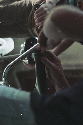 Close-up of a person adjusting a vintage car’s chrome fender mirror, visible through a rain-spotted windshield. Reflections a...