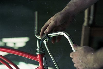 Close-up of hands adjusting a vintage bicycle’s handlebar stem, likely mid-1970s. Chrome details and red frame suggest classi...