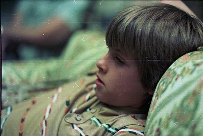 Close-up of a child resting on a camouflage-patterned jacket, likely mid-20th century. Soft focus and vintage film grain sugg...