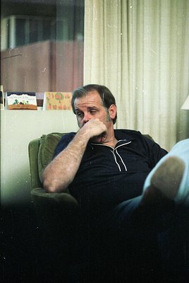 Vintage indoor portrait of a man in contemplative pose, seated in a green armchair. He wears a dark sweater and light-colored...