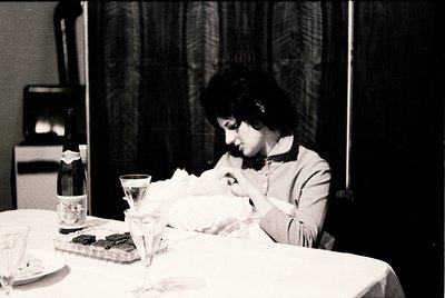 Black-and-white candid of a woman seated at a formal table, engrossed in writing. Mid-20th century attire and vintage typewri...
