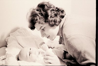 A tender black-and-white portrait of a woman cradling a newborn, likely from the 1950s–1960s. The woman’s hairstyle and cloth...