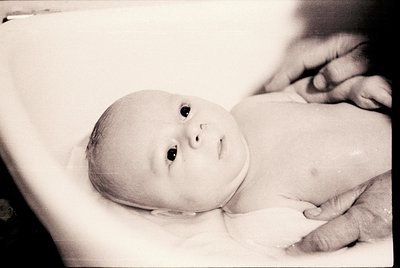 Vintage black-and-white portrait of an infant cradled in an adult’s arms, likely mid-20th century. Soft focus highlights tend...