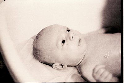 Black-and-white portrait of an infant in a hospital bassinet, likely mid-20th century. Soft focus highlights delicate feature...
