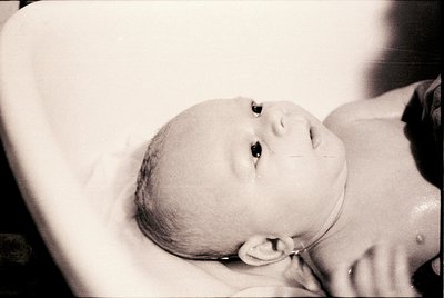 Black-and-white portrait of an infant in a swaddling cloth, likely mid-20th century. Soft focus highlights delicate features ...
