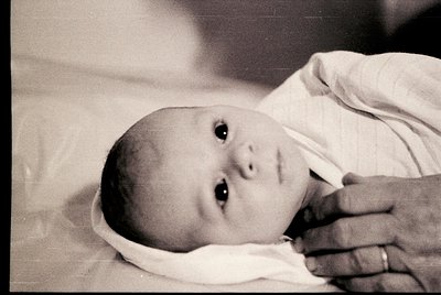 Black-and-white candid of an infant swaddled in a diaper, lying on a flat surface with one hand gently resting on their foreh...