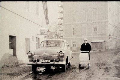 Vintage black-and-white street scene featuring a **ZIS-154** (Soviet-era car) parked on a muddy road. A woman in winter attir...