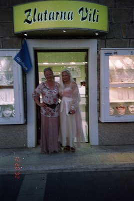 Two women pose outside a vintage jewelry shop, "Zlatarna Vili," in Bulgaria’s 1970s–80s era. The woman on the left wears a fl...