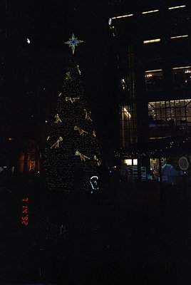 Vibrant nighttime cityscape featuring a towering, illuminated Christmas tree adorned with golden ornaments and a star-topped ...