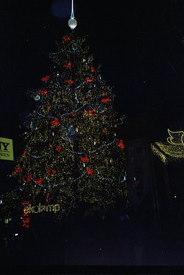 Elaborate gold-toned Christmas tree adorned with red baubles and reflective ornaments, illuminated against a dark backdrop. B...