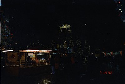 Vintage nighttime street scene with illuminated holiday decorations and a vintage camera timestamp (7:14:38). Decor includes ...