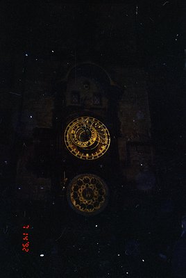 Vintage illuminated clock tower face with golden Roman numerals and decorative floral pattern, captured from below. Reflectio...