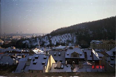 Vintage aerial view of a snow-covered European cityscape, likely . Residential rooftops and terraced hillsides frame a distan...