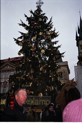 Vintage Christmas scene featuring a towering, elaborately decorated pine tree adorned with golden ornaments and a large reind...