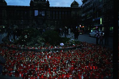 A memorial display of red candles and flowers arranged in a grid pattern on a city street at night, likely honoring a tragic ...