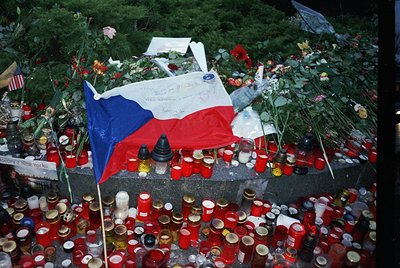 Memorial tribute featuring Czech flag, candles, and floral arrangements. Likely post-2016 terrorist attack in Prague. Crowd-s...