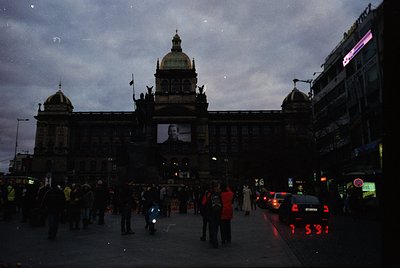 Neoclassical building façade with domed central tower, flanked by smaller domes, illuminated by large portrait projection. Ur...