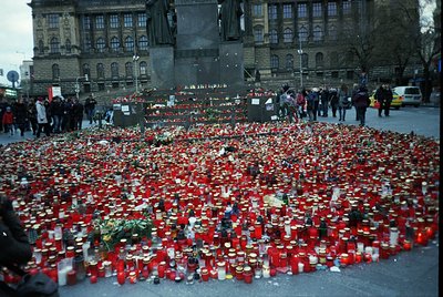 Memorial tribute with thousands of red candles and flowers arranged in a circular pattern on pavement, likely honoring victim...