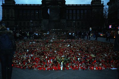 Memorial tribute featuring thousands of red roses and candles arranged in a dense, heart-shaped pattern on a city plaza. Surr...