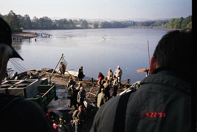 Vintage fishing scene on a muddy pier by a calm lake, with workers in heavy jackets and hats handling nets. Green utility tru...