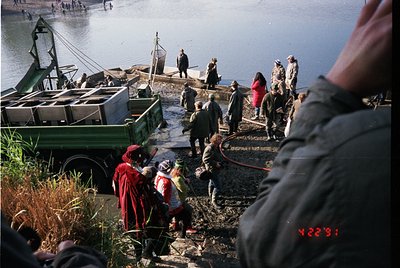 Vintage fishing scene with group unloading nets from a green truck near a waterfront. Mid-20th century attire and equipment s...