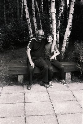 A man and woman pose closely on a wooden bench in a birch forest, likely 1970s–1980s. The man wears a striped polo shirt and ...