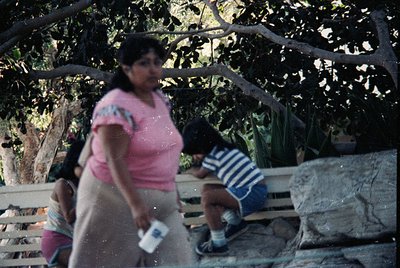 Vintage outdoor scene featuring a woman in a pink blouse and light-colored skirt holding a white object, possibly a book or p...