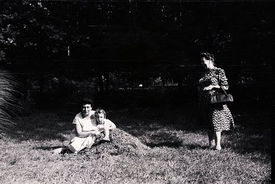 Mid-20th century black-and-white photo: two seated women (mother and child) in a grassy garden, one holding a small animal; a...