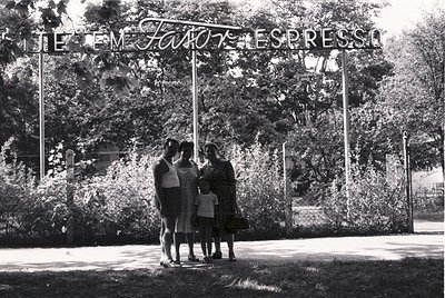 Mid-20th century black-and-white photo: Four people pose under a sign reading *"TEM FAVOR, ESPRESSO"* (Portuguese for "Please...