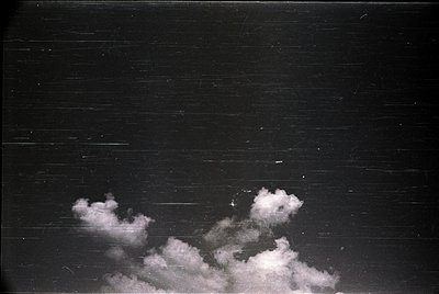 High-contrast black-and-white shot of dramatic cumulus clouds against a dark sky, framed by horizontal wooden planks. Likely ...