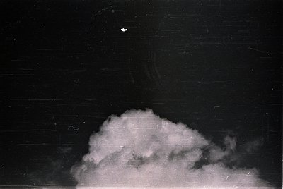 Vintage black-and-white photo of a lone bird silhouetted against a dense, low-hanging cloud formation. The composition emphas...