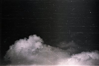 Vintage black-and-white photo of dense, low-hanging clouds against a dark sky, likely captured with early film grain. The tex...