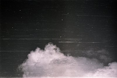 Vintage black-and-white photo of dense fog obscuring a horizontal wooden structure, likely a fence or wall. Streaks suggest m...