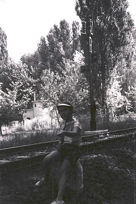 Mid-20th century black-and-white photo: man in uniform (likely military or railway worker) perched atop a train rail, holding...