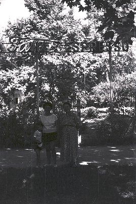 Reflection of a child in a mirrored glass door, framed by lush greenery and a sign reading "Kinderpark" in Cyrillic. Likely E...