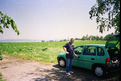 Vintage green hatchback (likely a Škoda Fabia or similar) parked beside a rural road, with a man in a dark polo shirt and jea...
