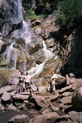 Group of 10 posing near a cascading waterfall in a rocky canyon, likely mid-20th century outdoor adventure. Casual attire sug...