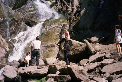 Group of five people exploring a rocky riverside waterfall trail, likely mid-1990s. Casual summer attire suggests leisure act...