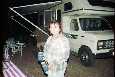 Vintage camper van parked under a canopy at night, featuring classic 1980s design with pop-up roof. Woman in plaid shirt hold...