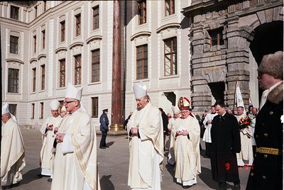 Neoclassical courtyard procession featuring clergy in liturgical vestments, likely 1970s–1990s. White robes, miters, and cros...