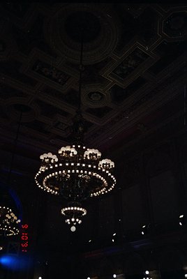 Art deco chandelier with geometric ceiling patterns, likely from a 1920s–1940s European café or theater. Intricate crystal de...