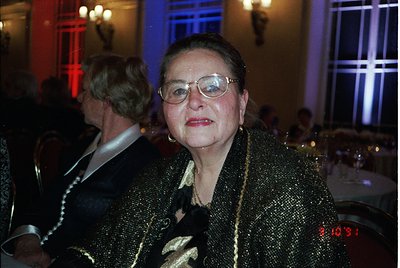 Elegant woman in a shimmering gold sequin coat, framed by dim indoor lighting with a clock displaying 20:31. Formal evening a...