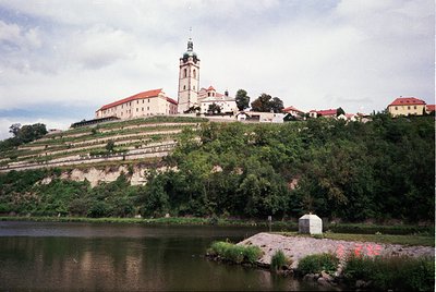 Historic hilltop fortress with Baroque-style church tower and vineyard terraces overlooking a river. Architectural details in...