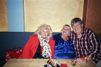 Vintage family portrait featuring three adults in casual indoor setting. Woman on left wears bold red blazer with white fur c...